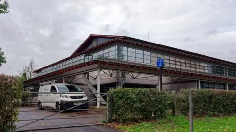 Peterborough Crown Court: The front of a white building with angled roof and a white van parked outside blue door and black-framed glass windows