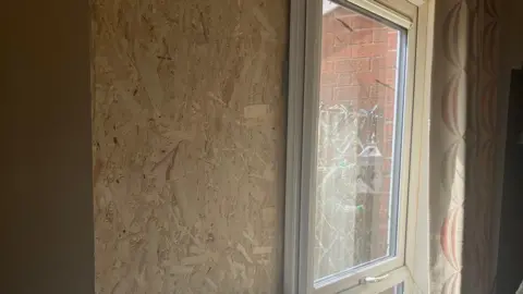 A piece of wood is placed over a smashed window. to the right of the wood a smashed window pane can be seen.