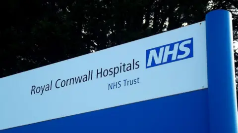 A close-up of a blue and white sign outdoors which says "Royal Cornwall Hospitals NHS Trust"