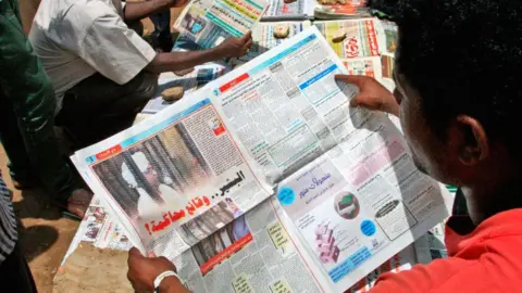 Getty Images A Sudanese man reads the newspaper headlining the court appearance of deposed military ruler Omar al-Bashir, August 2019