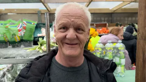 Andrew Wickham is smiling at the camera with food in the background.