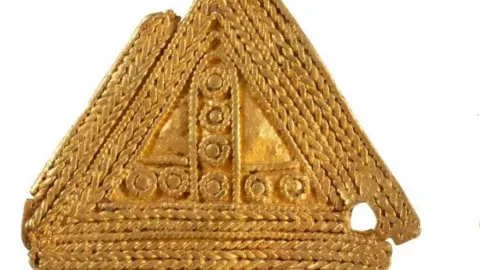 A gold plated triangular Anglo-Saxon gold object adorned with an intricate twisted gold wire filigree design.