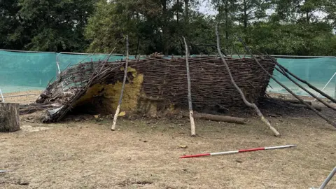 Tom Jackson/BBC A broken wicker line of fencing with trees branches laid against it, propping it up. Metal fences, covered in green mesh, seal off the area. Trees are in the background.