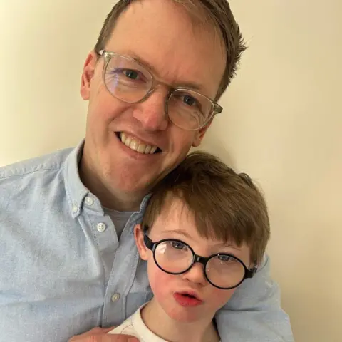 Family A man wearing glasses holding his son who is also wearing glasses 