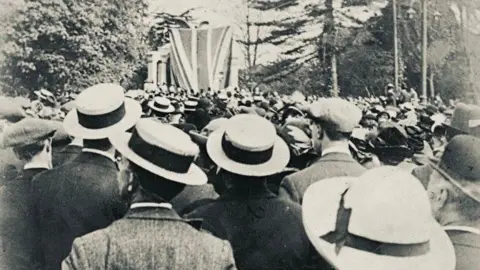 Mike Thomas A black and white image of a large crowd gathered in front of the new Titanic Engineers' Memorial in 1914. The memorial itself is covered by a large Union Jack as it is yet to be unveiled.