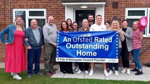 Staff from Amersall children's home displaying a banner saying it is an "outstanding" home