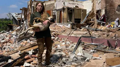 12 Guardians A woman holds a dog in the rubble of a house
