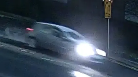 A blurred picture of a car, with its headlights on, driving down a road.