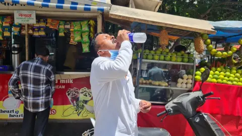 BBC A man drinks water on a hot afternoon in Mumbai city
