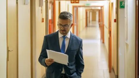 Matthew Goddard/BBC News presenter Zbigniew Luczynski stands in a corridor reading notes