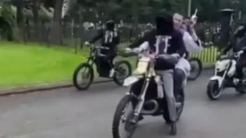 priest sprinking holy water behind bike rider