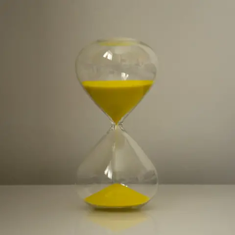 Ali Waggie An image of a large hourglass with yellow sand inside