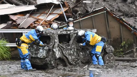 Reuters Police officers conduct search and rescue operation around a destroyed car at a mudslide site caused by heavy rain at Izusan district in Atami, west of Tokyo, Japan, 4 July 2021