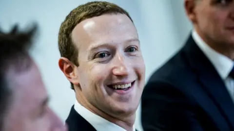 Getty Images Facebook founder Mark Zuckerberg smiles at the camera in this close-up shot of a group, with other members obscured by the framing