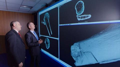 Two men stare at in-depth images of a bone on a screen