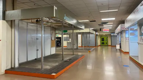 A row of empty market stalls. Metal shutters are closed across stalls 