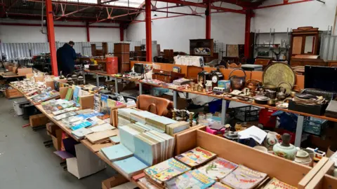 The auction hall with rows of old goods, from comics to antique safes and old electronics.