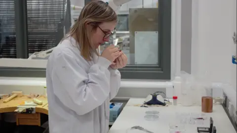 UWE Sofie Boons studies a gemstone in her laboratory. She is wearing a white lab coat and glasses