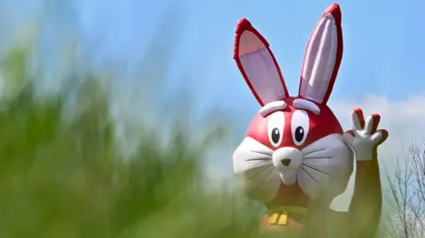 Getty Images A large inflatable Easter Bunny, partially obscured by a tree, is puctured waving. 