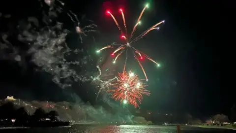 BBC Red and green fireworks light up the sky over Mooragh Park, you can see the lake in the foreground.