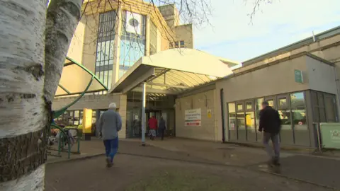 An exterior shot of Dr Gray's on a cloudy day showing unidentified patients/ visitors walking towards a set of sliding doors to access the main entrance