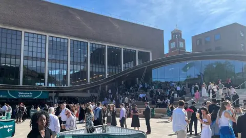Graduation Day at the Forum at the University of Exeter with groups of people chatting and a Welcome to Graduation sign in the bottom left.