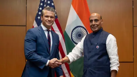 Pete Hegseth/Twitter US Defence Secretary Pete Hegseth (L) and India's Defence Minister Rajnath Singh shake hands after meeting in Kuala Lumpur, with their countries flags behind them. 