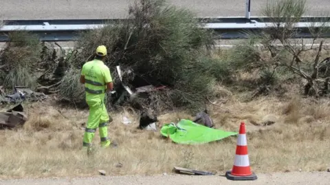A Spanish worker wearing fluorescent yellow stands at the scene of the crash in Spain where Diogo Jota was killed