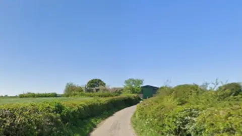A rural country lane in Rotherham with hedges and fields either side and blue sky above