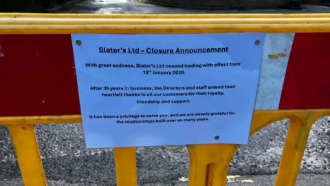 A white piece of paper attached to a yellow, red and white barrier notifying people of the closure of Slater's.