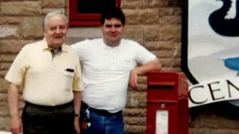 Fred White and his son Bryan. They stood together to take pictures, and Brian leaned on the red mailbox. Fred's white hair is short, wearing yellow short -sleeved T -shirts. Brian wore a white T -shirt and blue jeans. 