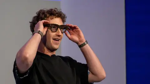 Bloomberg via Getty Images Mark Zuckerberg, wearing a black t-shirt and smiling, interacts with a pair of Meta Ray-Ban Display glasses in front of an audience.