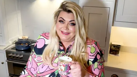 Getty Images Gemma Collins stands in a kitchen holding a cup of tea and smiling