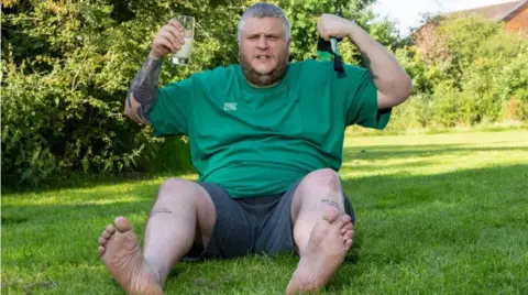 World toe wrestling champion Ben Woodroffe sat on grass bare foot in a green T-shirt