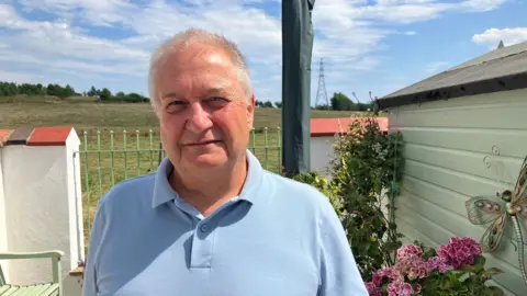 Photograph of John Hinckley from Atherton. He is pictured in the back garden of his home, with open farmland and trees in the background.