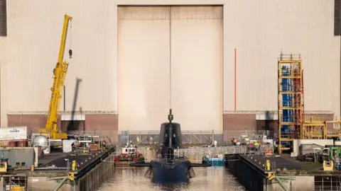 BAE SYSTEMS PLC Front-on view of BAE hangar with HMS Agamemnon while it is being hoisted into the water.