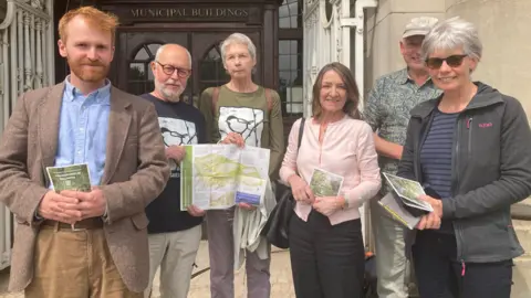 Campaigners from the Danes Moss Trust stand outside a council building holding up leaflets expressing their objection to the proposals.