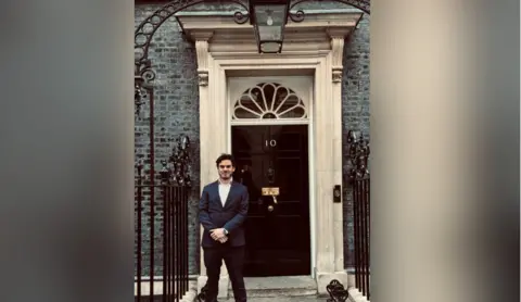 Paul Humpherson in a dark suit outside of 10 Downing Street. He is smiling.