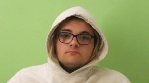 Guernsey Police A police picture of Jessica Garnham-Burton. She is wearing a white hooded jumper with the hood up. She has blonde hair and black glasses. 