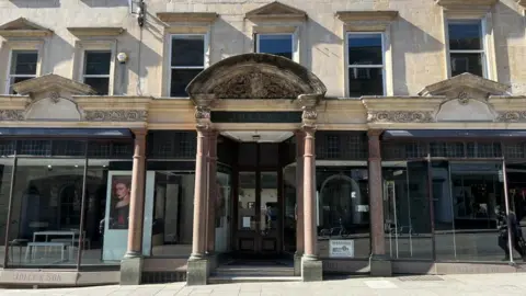 The now empty Jolly's department store in Bath, pictured from outside. The windows are bare apart from one stand with a poster of a female model on it.