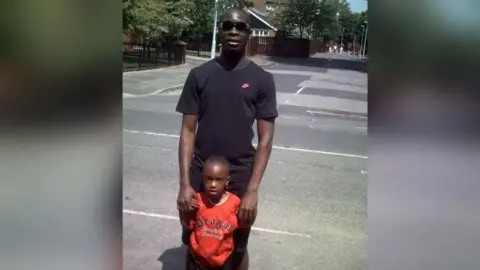 Prince as a young child, pictured in a red tshirt with his uncle Kemoy Walker stood behind him wearing sunglasses