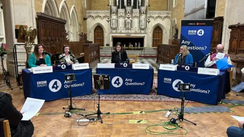 The Any Questions? panel in a church in Porthcawl, featuring Sioned Williams, Eluned Morgan, Alex Forsyth, Mimms Davies and a man in a purple vest jumper 