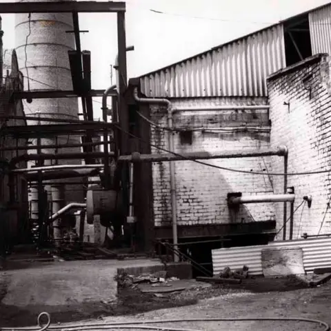 National Mining Museum Scotland A whitewashed brick building with a corrugated roof stands next to the bottom of a chimney tower in this black and white picture.