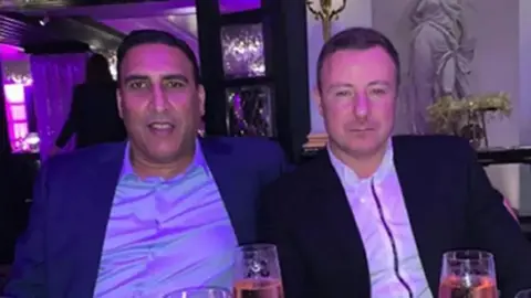 Police handout Left to right: Nasar Ahmed wearing a purple shirt and navy suit jacket and Jonathan Cassidy wearing a white shirt and black suit jacket with champagne glasses on a table in front of them.