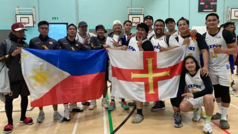 Two basketball teams - one of them is holding a Filipino flag and the other is holding a Guernsey flag 