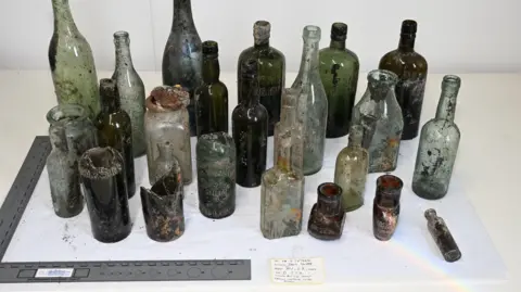 ODAIT A number of glass bottles of various sizes and colours on a white background. 