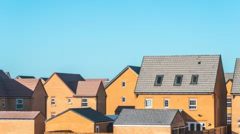 Getty Images Brown brick homes bathed in light in a new development. The sky is pure blue with not a cloud in sight.