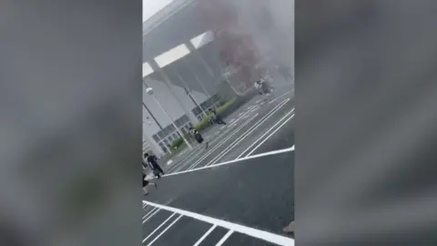 People flee from a building with smoke rising in the background