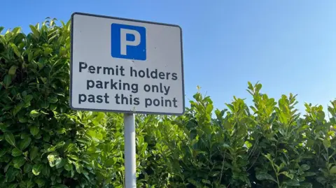 Gill Edgar A square shaped parking sign on a pole, showing  a blue and white logo and the words 'Permit holders parking only past this point'