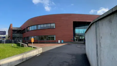 The Dumfries and Galloway College building with a curved brick frontage and a wide tarmac path leading to it